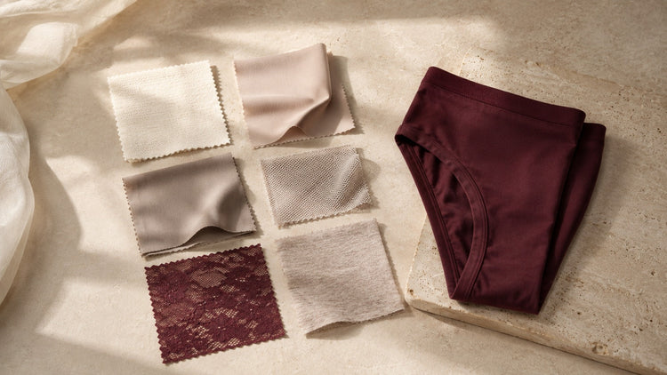Cotton, modal, microfiber, mesh and lace swatches arranged beside folded underwear on a warm ivory surface.
